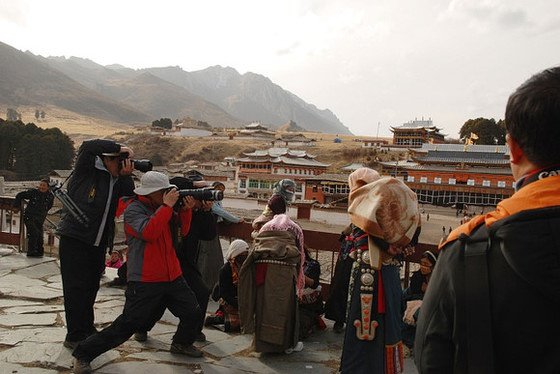 地點：四川郎木寺左手邊山坡上的廟前描述：沿著右手走不了幾步，映入眼簾的場景背著孩子的藏族女人，被三個“影友”直面拍，請特別注意欄杆邊站著的藏族姑娘